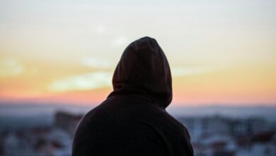 A solitary figure in a hoodie gazes at a vibrant sunset from a rooftop, creating a peaceful silhouette.