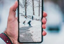 Hand holding smartphone displaying a winter scene with people walking on snow-covered path.