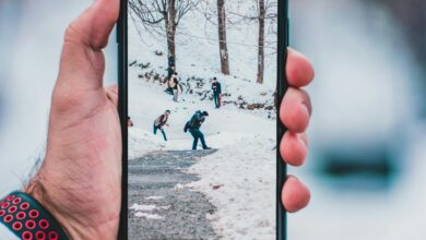 Hand holding smartphone displaying a winter scene with people walking on snow-covered path.